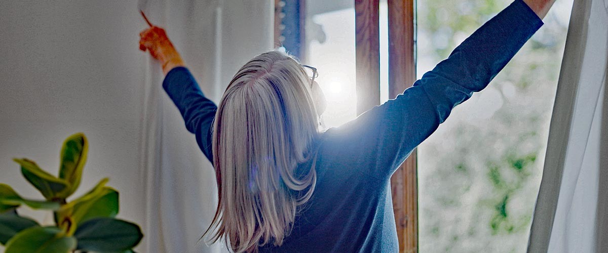 Elderly woman in home, opening curtains and getting ready for the day with sun, light and fresh air. Morning routine, retirement and senior person at window in apartment, housework and chores in room